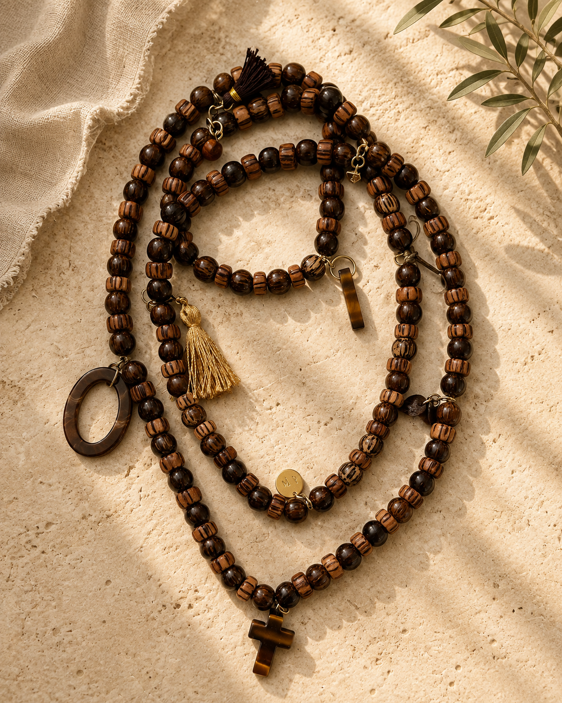 Lange ketting met houten kralen, goudkleurige details, kwastjes en hangers, een kruisje van tijgeroog